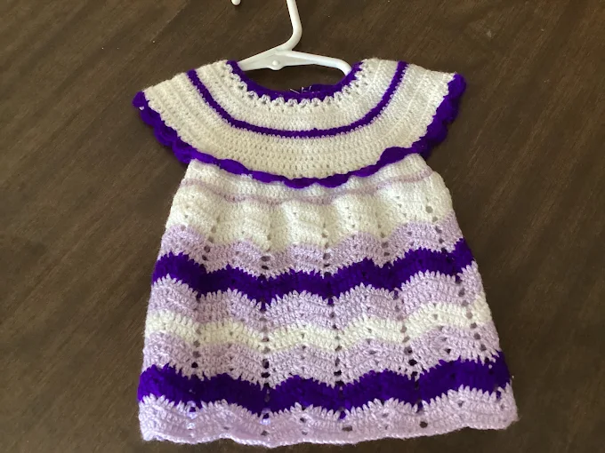 Hand-crocheted purple and white ripple-stitch doll dress on a hanger